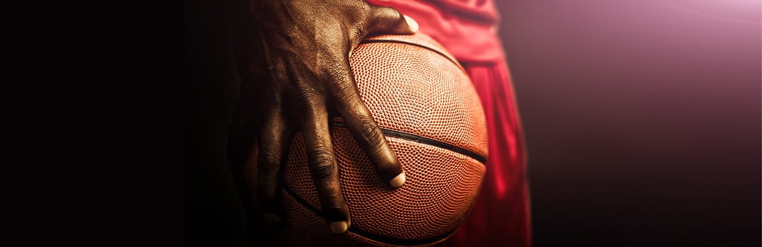 Athlete holds a basketball against his hip with one hand. 